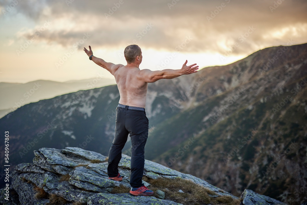 Bare-chested middle-aged man on top of rocky mountains Bare-chested middle-aged man on top of rocky mountains