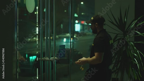 Guard or security worker walking , closing door and turning  plate with open closed sign at night . Guard dressed security uniform working inside storage or shop . Concept of night shift work