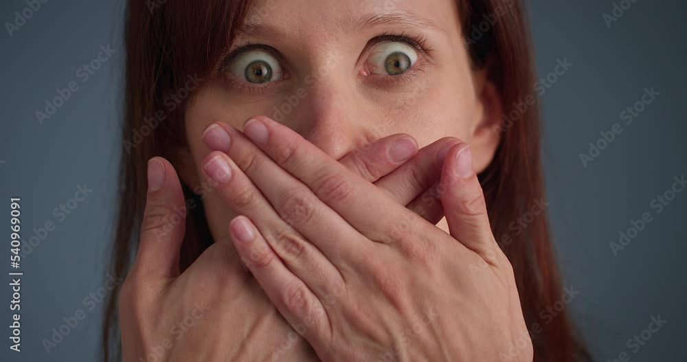 Extreme close-up shot of woman in shock covers mouth with both hands crossing Extreme close-up shot of woman in shock covers mouth with both hands crossing