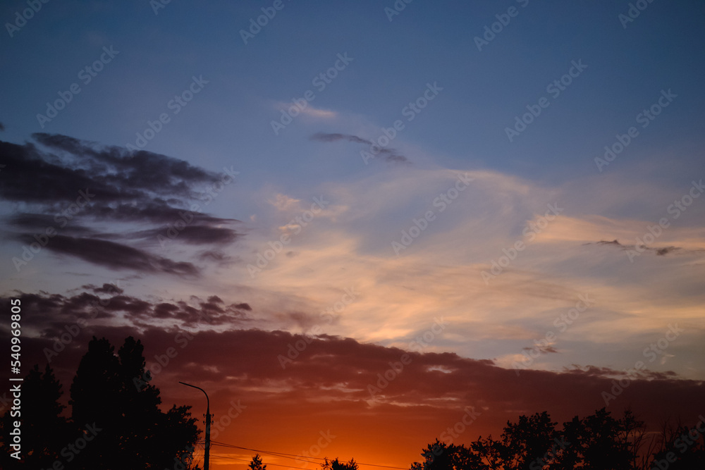 Obraz premium The morning glow illuminates the clouds on a beautiful colorful sky above the silhouettes of trees and a pillar at dawn