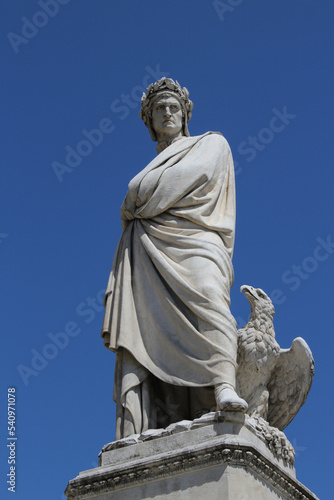 White marble statue of Italian poet Dante Alighieri, by sculptor Enrico Pazzi, in Piazza Santa Croce, Florence, Italy. Literature concept. Vertical full length shot with blue sky on background. photo
