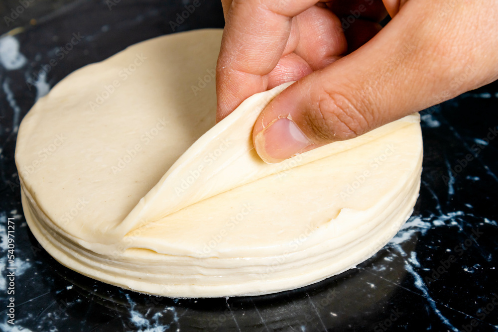 Preparation of pastry with puff pastry separating one of the doughs from a set of them with the hand of a white woman. Mention food preparation in the kitchen at home, fast and practical food. Preparation of pastry with puff pastry separating one of the doughs from a set of them with the hand of a white woman. Mention food preparation in the kitchen at home, fast and practical food.