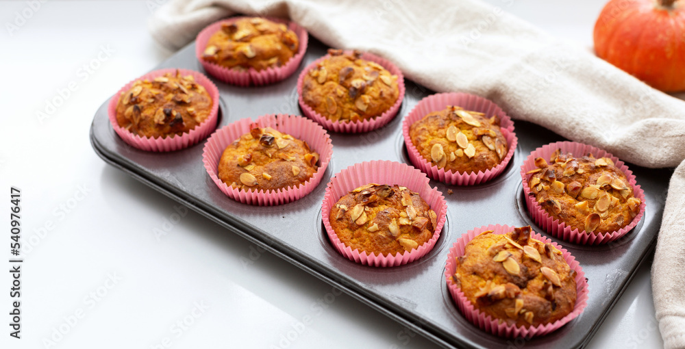 Homemade pumpkin muffins with pumpkin seeds and walnut pieces. Fall baking for Thanksgiving and Halloween. Cupcakes in baking dish on linen napkin. Selective focus. Close up. Copy space