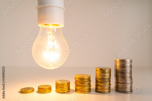 Lit light bulb with coins beside it. Increase in energy tariffs. Efficiency and energy saving. 
