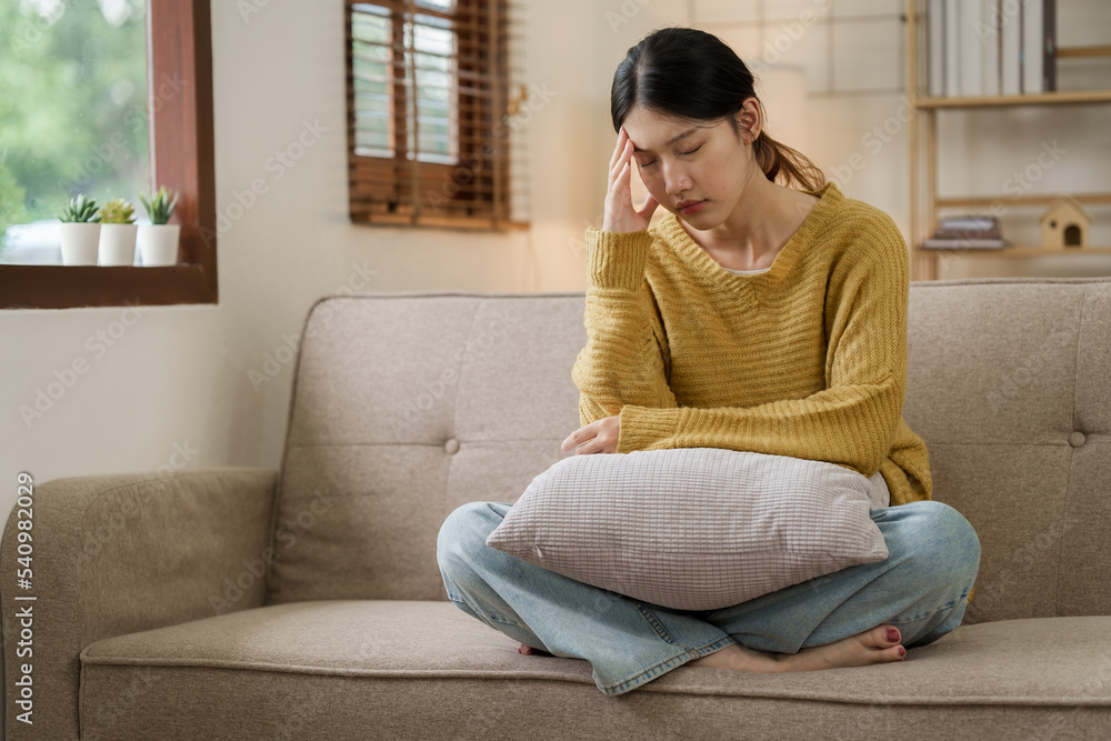Obraz premium Asian woman with a headache and stress while sitting on the sofa at home