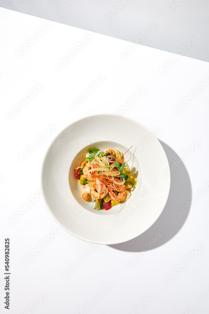 Elegant food - salad with shrimp and avocado on white table with harsh shadow. Flashy food concept. Seafood salad with shrimp, tomatoes and avocado on white plate with sunlight. Elegant food - salad with shrimp and avocado on white table with harsh shadow. Flashy food concept. Seafood salad with shrimp, tomatoes and avocado on white plate with sunlight.
