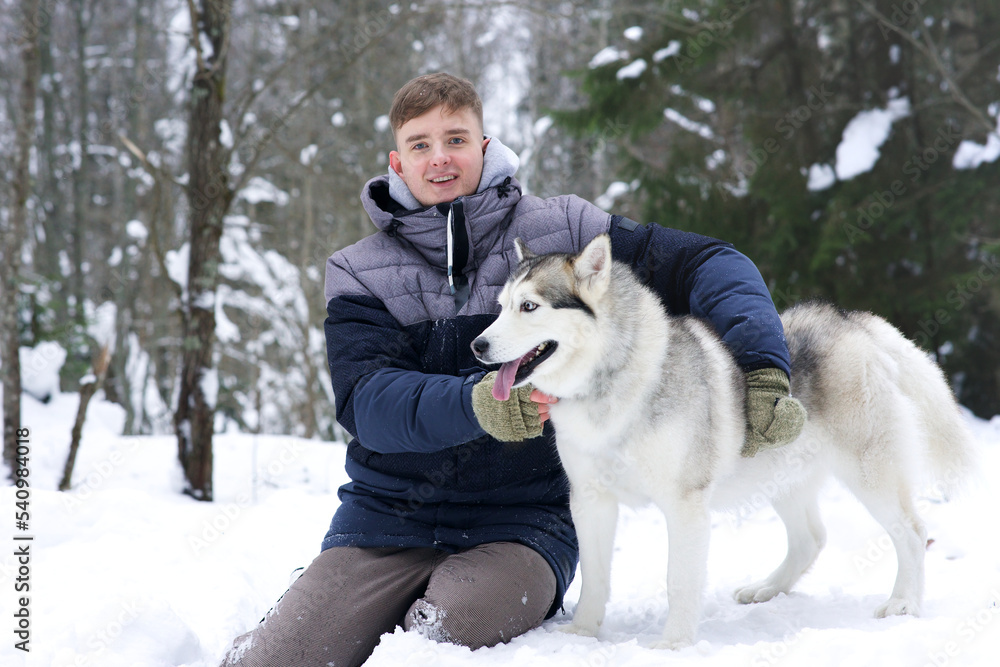 Handsome guy, young happy man walking with husky dog in snowy winter cold forest in snow looking at camera and smile. Handsome guy, young happy man walking with husky dog in snowy winter cold forest in snow looking at camera and smile.