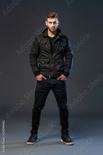 Portrait of cool looking handsome young man in casual wear standing against dark background. © Dmytro Panchenko