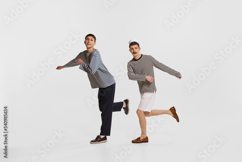 Portrait of two young boys, sailor, seamen in striped shirts walking on a dance isolated over white background