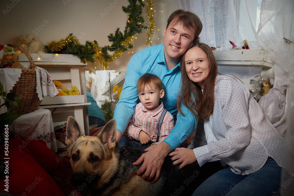Happy family with father, mother and small kid son together in the room decorated for Christmas and New Year and big dog german shepherd or russian eastern european shepherd