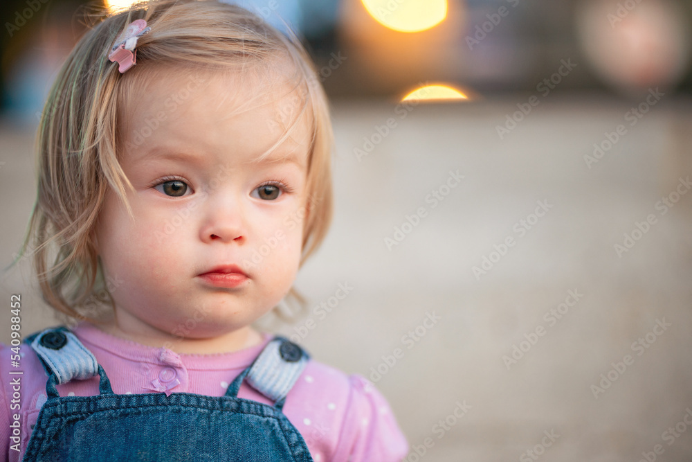 A cute little girl is sitting on the steps of the pier on the seashore. Young blonde in the rays of the setting sun. Street portrait of a little girl on a walk A cute little girl is sitting on the steps of the pier on the seashore. Young blonde in the rays of the setting sun. Street portrait of a little girl on a walk