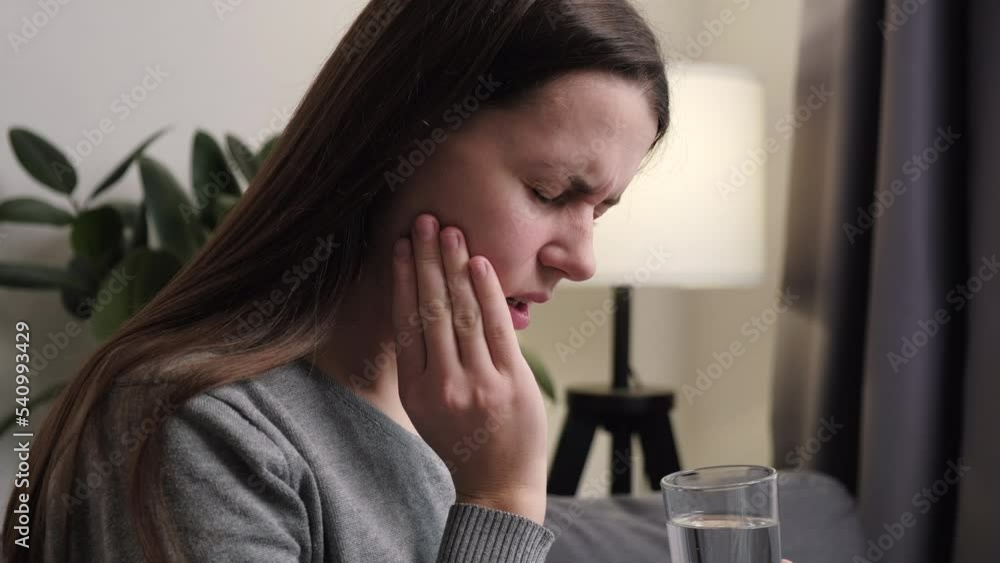 Young woman suffering from toothache, girl holding glass of water with ice touch cheek, face expression ache or feel pain, sensitive molar teeth, inflammation when drink cold, healthcare concept Young woman suffering from toothache, girl holding glass of water with ice touch cheek, face expression ache or feel pain, sensitive molar teeth, inflammation when drink cold, healthcare concept