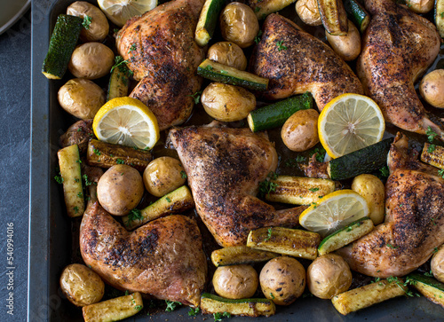Baked chicken legs with potatoes and zucchini on a baking tray
