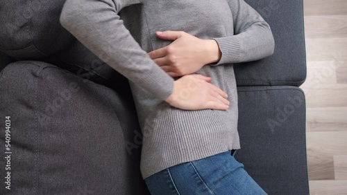 Top view of sick woman suffering from menstrual pain. Girl with hands squeezing belly having painful stomach ache or period cramps lying on sofa. Abdominal pain, gastritis and painful periods concept photo
