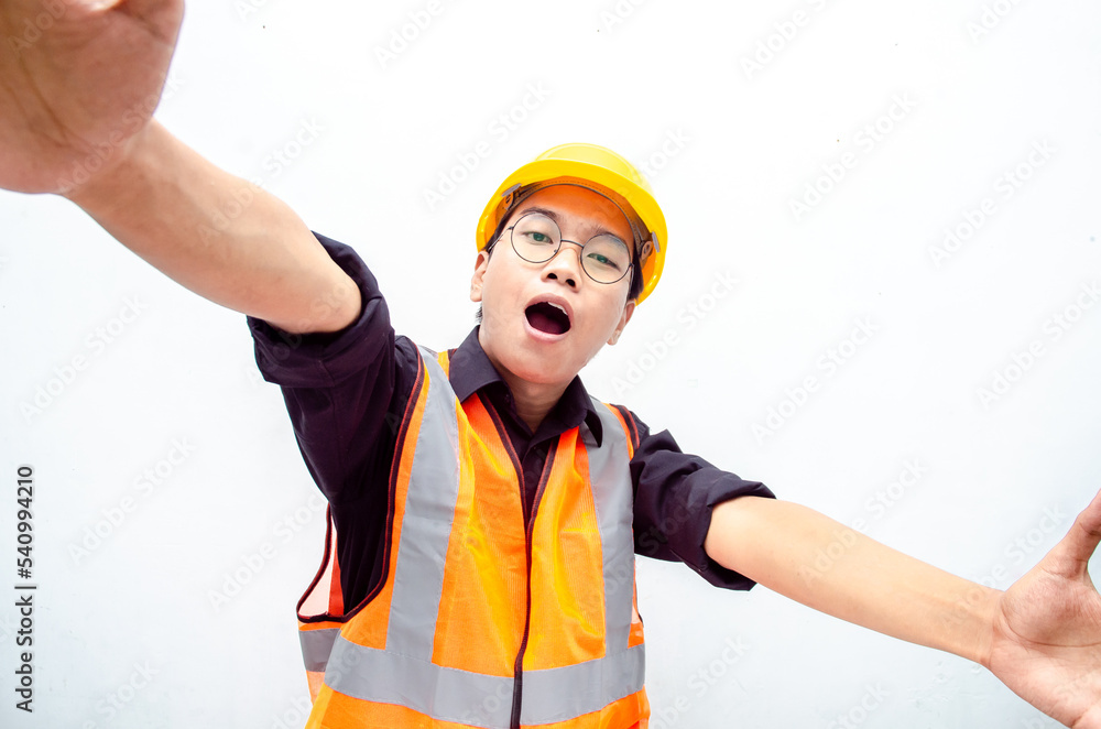 Portrait of a joyful male construction worker or engineer taking selfie and holding camera with hands over white background. asian male engineer open arms for a hug and giving surprise gesture. Portrait of a joyful male construction worker or engineer taking selfie and holding camera with hands over white background. asian male engineer open arms for a hug and giving surprise gesture.