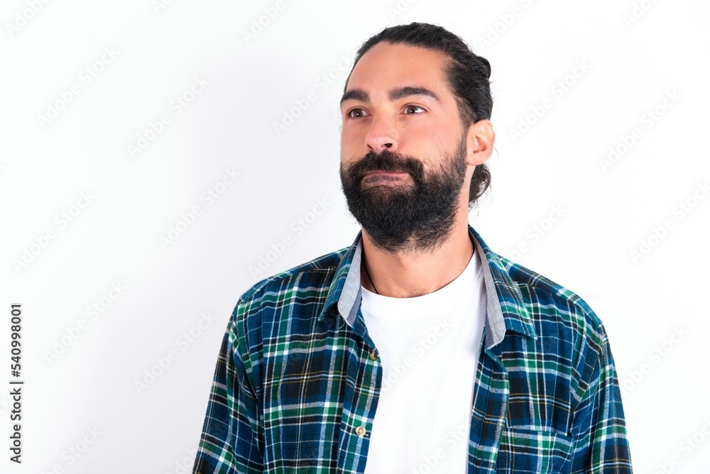 Amazed puzzled young bearded hispanic man wearing plaid shirt over white background , curves lips and has worried look, sees something awful in front. Amazed puzzled young bearded hispanic man wearing plaid shirt over white background , curves lips and has worried look, sees something awful in front.