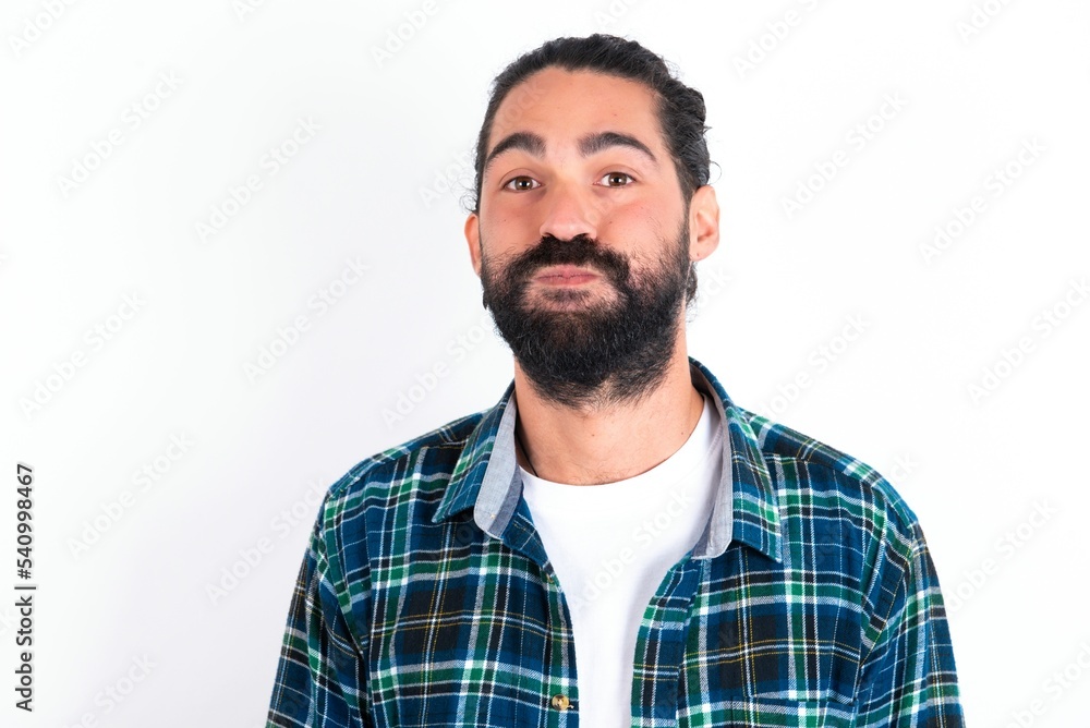 young bearded hispanic man wearing plaid shirt over white background puffing cheeks with funny face. Mouth inflated with air, crazy expression. young bearded hispanic man wearing plaid shirt over white background puffing cheeks with funny face. Mouth inflated with air, crazy expression.