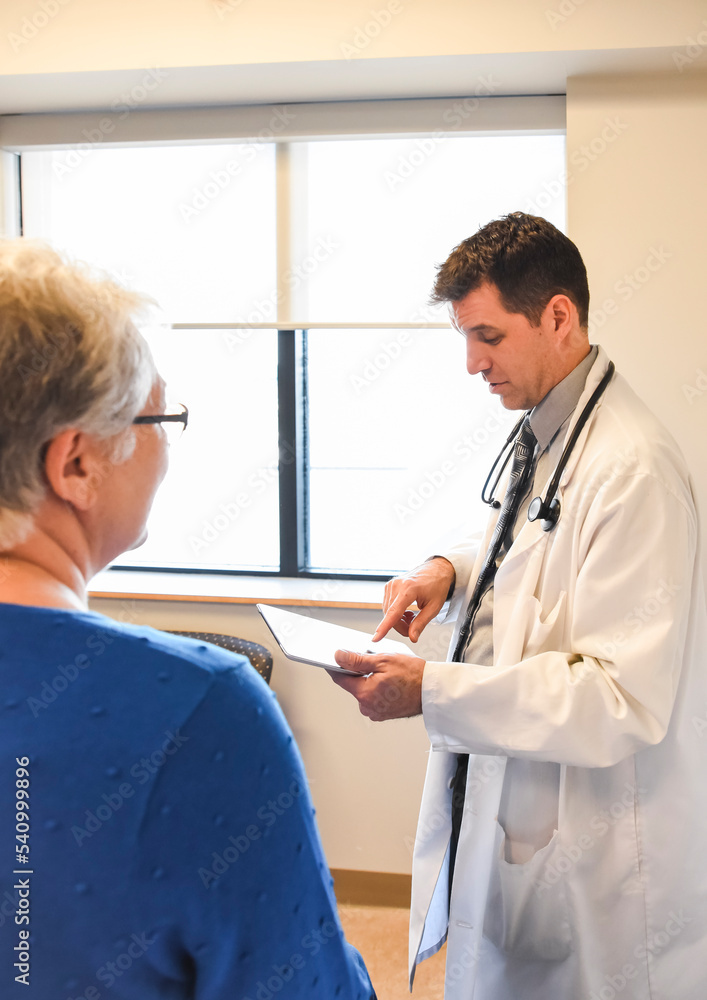 Doctor holding tablet speaking to older patient in a clinical setting. Doctor holding tablet speaking to older patient in a clinical setting.