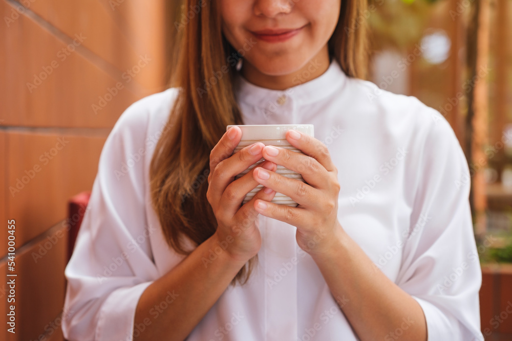 Closeup image of a young woman holding and drinking hot coffee in cafe Closeup image of a young woman holding and drinking hot coffee in cafe