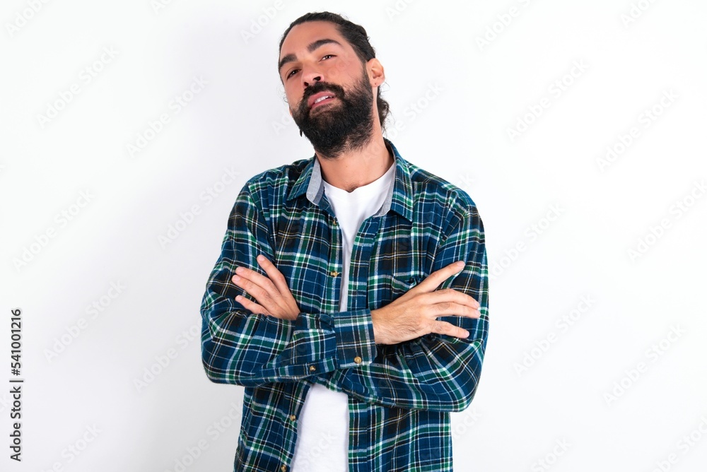 young bearded hispanic man wearing plaid shirt over white background frowning his face in displeasure, keeping arms folded, waiting for an explanation. young bearded hispanic man wearing plaid shirt over white background frowning his face in displeasure, keeping arms folded, waiting for an explanation.