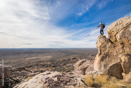 A young, male adventurer, standing on top of a granite cliff, points at something in the distance in the desertic landscape of PeÃ±oles, Chihuahua. photo
