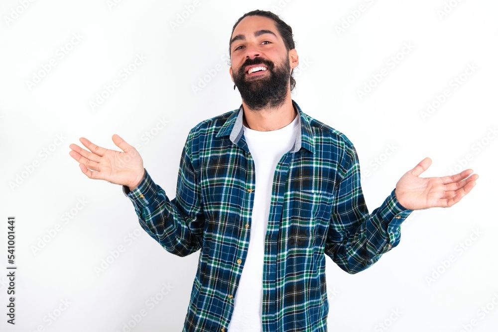 Fototapeta premium So what? Portrait of arrogant young bearded hispanic man wearing plaid shirt over white background shrugging hands sideways smiling gasping indifferent, telling something obvious.