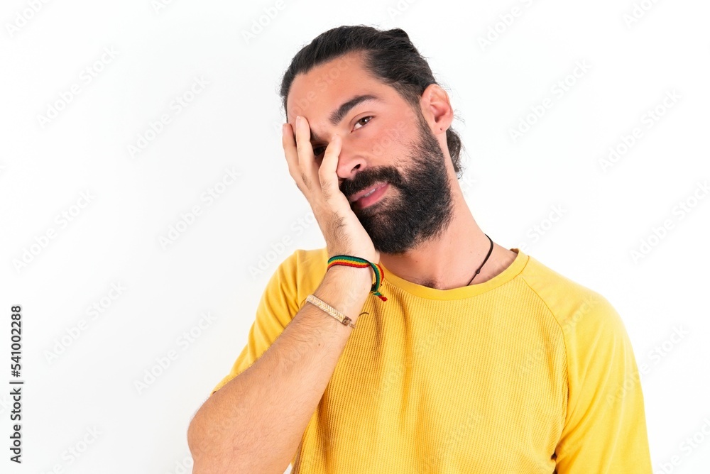 young bearded hispanic man wearing yellow T-shirt over white background makes face palm and smiles broadly, giggles positively hears funny joke poses young bearded hispanic man wearing yellow T-shirt over white background makes face palm and smiles broadly, giggles positively hears funny joke poses