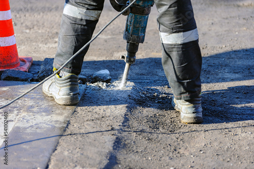 Foto A road worker breaks asphalt with an impact jackhammer at a construction site
