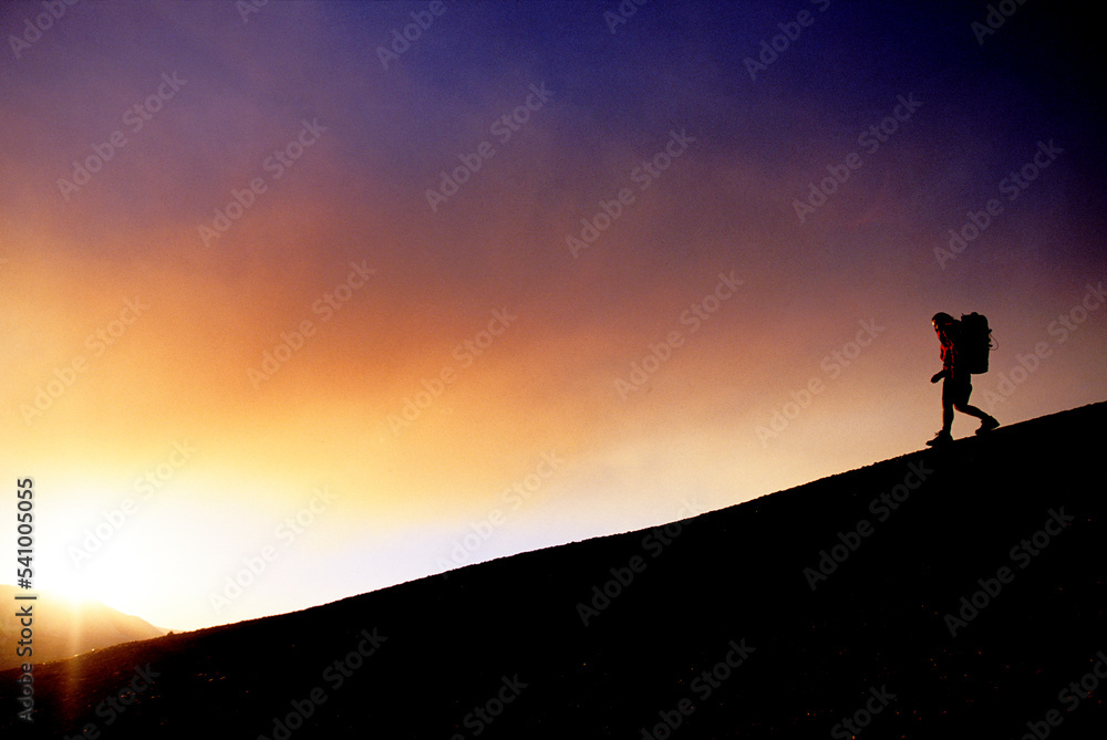 Silhouette of a person backpacking down a slope at sunset. Silhouette of a person backpacking down a slope at sunset.