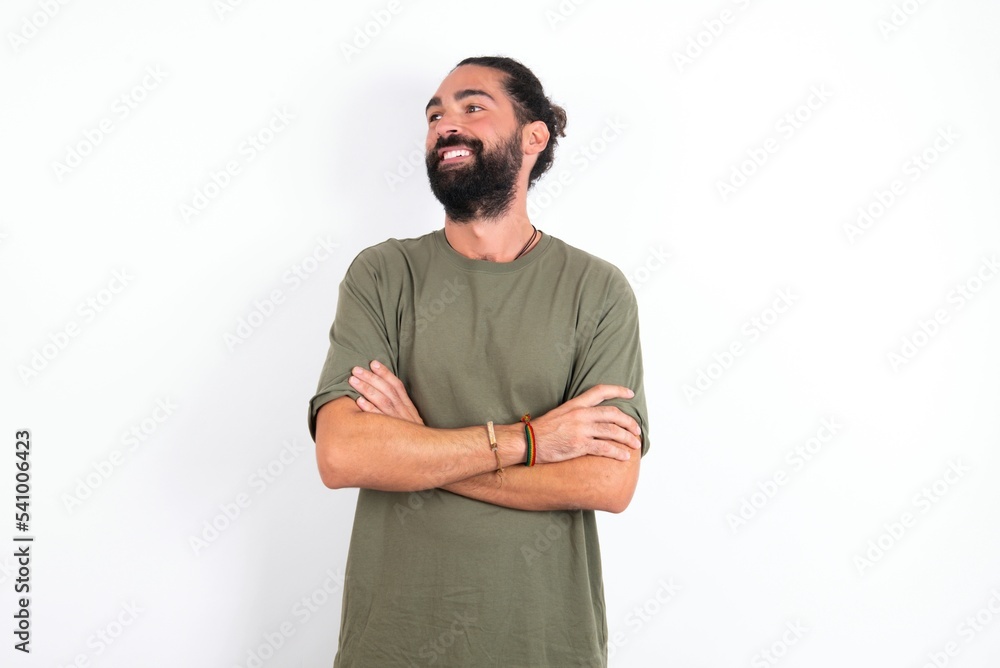 Fototapeta premium Dreamy rest relaxed young bearded hispanic man wearing green T-shirt over white background crossing arms, looks good copyspace