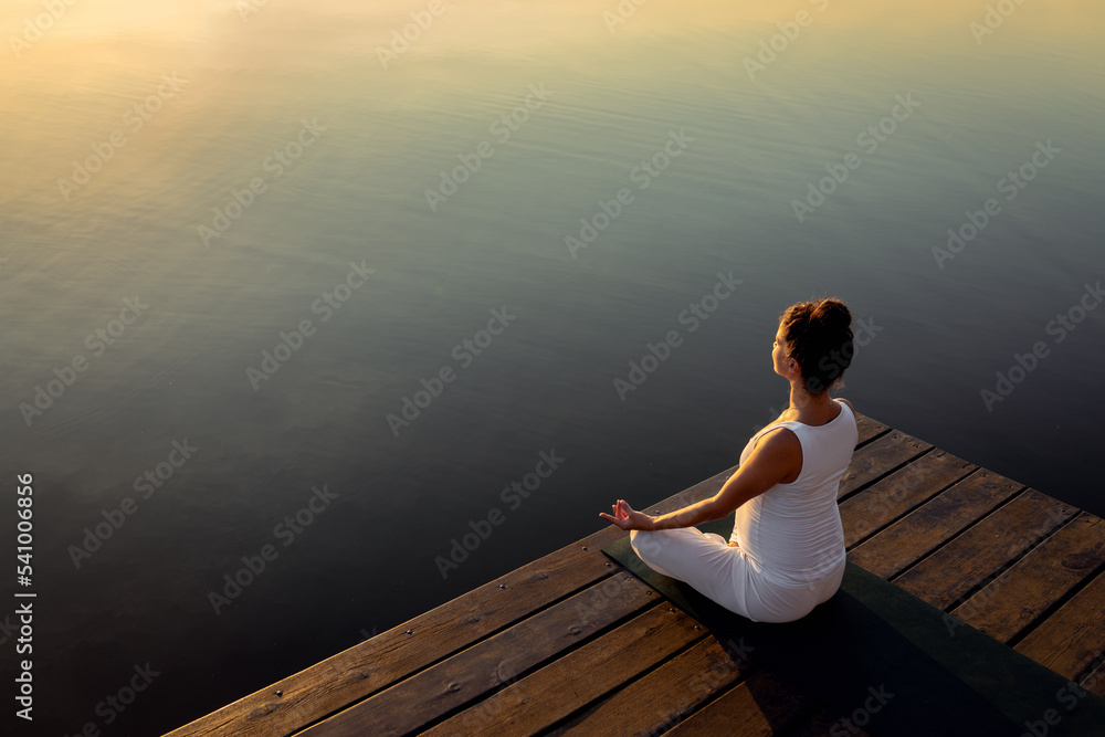 Pregnant woman doing yoga at lake during sunset.