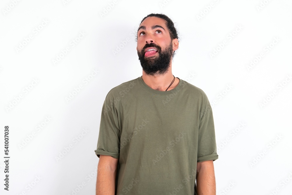 young bearded hispanic man wearing green T-shirt over white background showing grimace face crossing eyes and showing tongue. Being funny and crazy young bearded hispanic man wearing green T-shirt over white background showing grimace face crossing eyes and showing tongue. Being funny and crazy