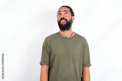 Fotografie young bearded hispanic man wearing green T-shirt over white background showing grimace face crossing eyes and showing tongue