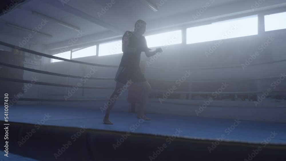 Kickboxer silhouette training in fighting club ring, slow motion wide shot. Young fighter gym workout, sportsman practicing kicks long angle view, slo mo Kickboxer silhouette training in fighting club ring, slow motion wide shot. Young fighter gym workout, sportsman practicing kicks long angle view, slo mo