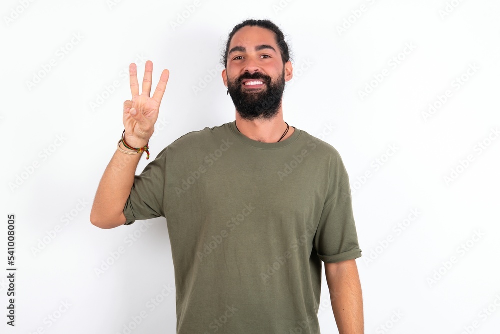 young bearded hispanic man wearing green t-shirt over white background showing and pointing up with fingers number three while smiling confident and happy. young bearded hispanic man wearing green t-shirt over white background showing and pointing up with fingers number three while smiling confident and happy.