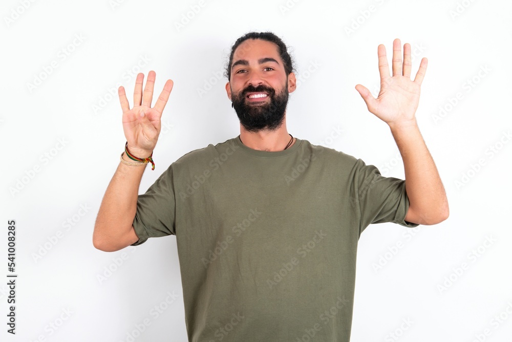 young bearded hispanic man wearing green t-shirt over white background showing and pointing up with fingers number nine while smiling confident and happy. young bearded hispanic man wearing green t-shirt over white background showing and pointing up with fingers number nine while smiling confident and happy.