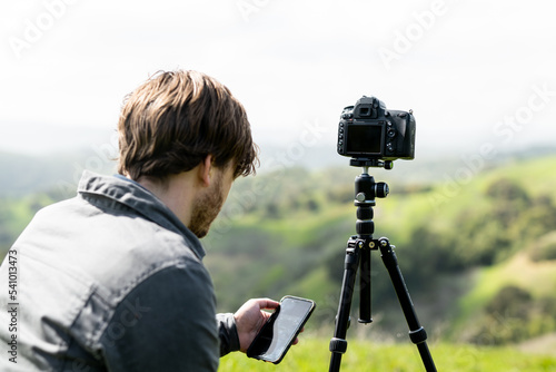 Person using smartphone app to control camera on tripod outdoors photo