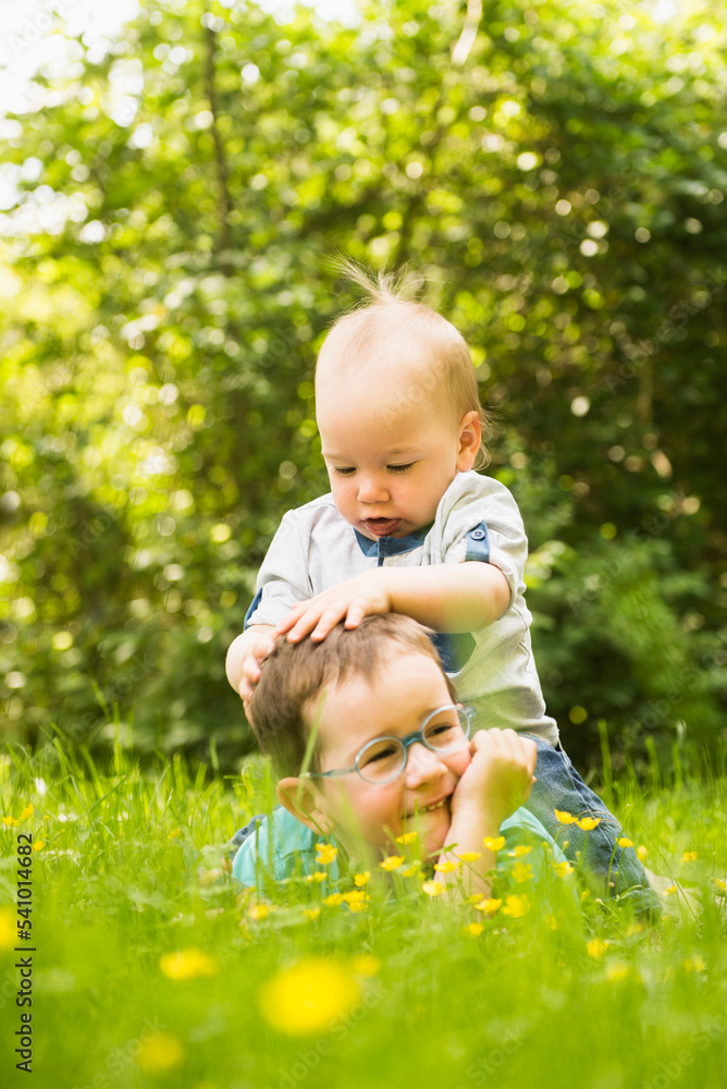Small boy sitting on his brother in the garden Small boy sitting on his brother in the garden