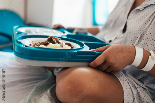 Young woman hospitalized in a bed. Holding hospital food tray. photo