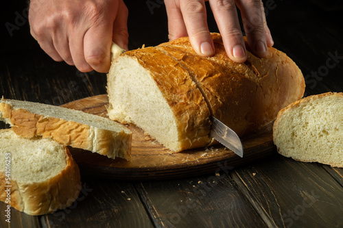 The chef cuts fresh bread with a knife on a kitchen cutting board. Healthy food and traditional bakery concept
