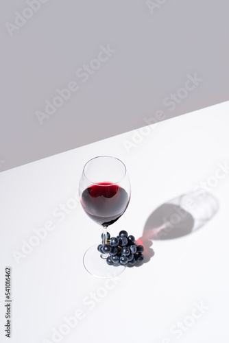 Copa de vino tinto y racimo de uvas negras sobre fondo gris	 photo