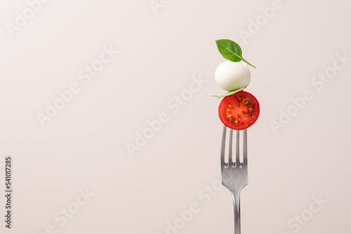 Fork with tomato, mozzarella cheese and basil. Caprese salad on fork close up view. Italian food concept photo