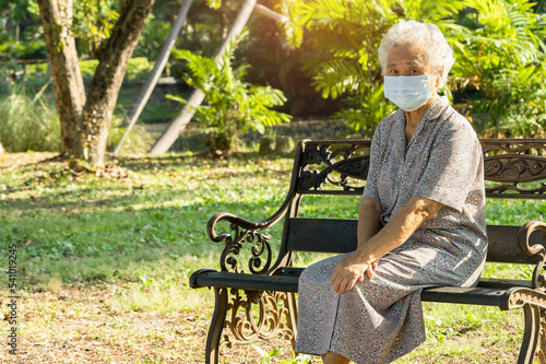 Asian elderly woman depressed and sad with mask for protect covid 19 sitting back on bench in autumn park.