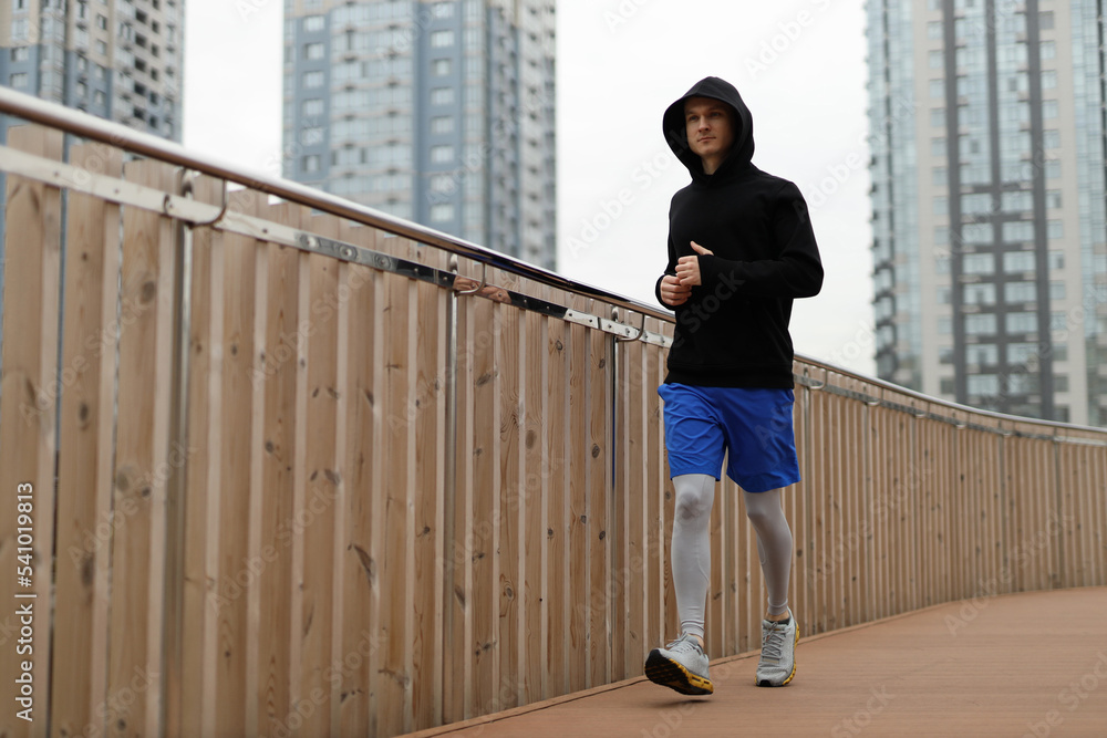 A man in warm sportswear walks along a wooden bridge in outdoor. Sporting walk workout in city.