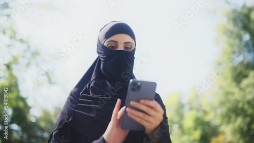 Middle-eastern woman in burqa texting on smartphone outdoor, mobile application photo