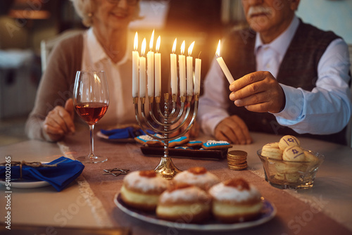 Close up of senior couple lighting candles while celebrating Hanukkah at home.