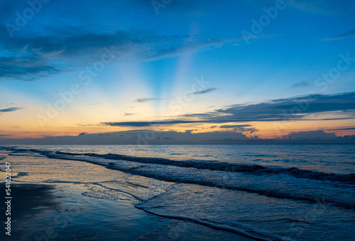 Sun rays coming from behind clouds at sunrise over the ocean at the beach