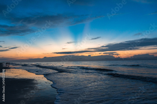Sun rays coming from behind clouds at sunrise over the ocean at the beach