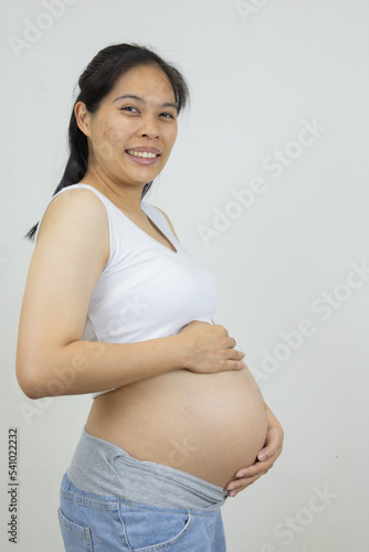 Asian pregnant woman holding her belly with a happy smile, eagerly awaiting the birth of her unborn baby.