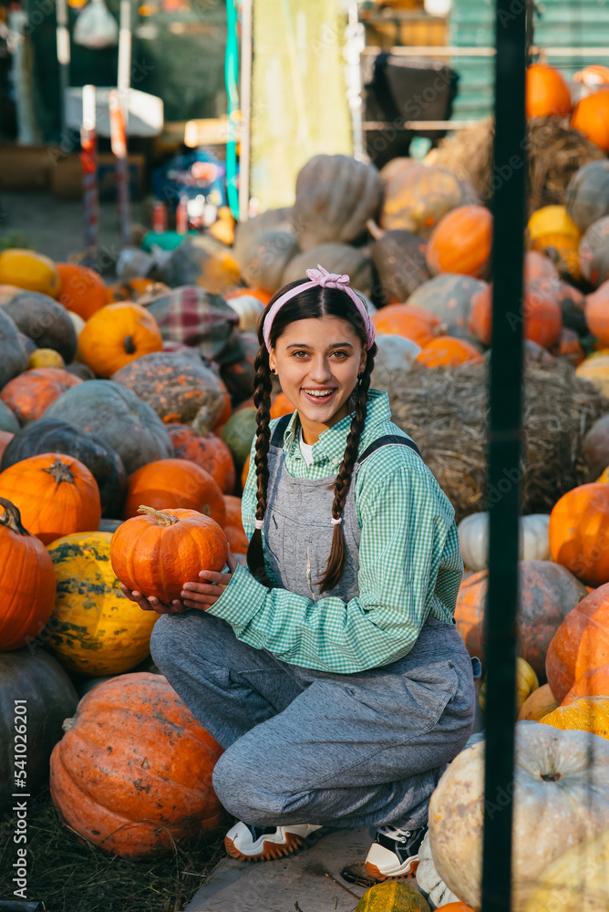 Farmer woman in a denim jumpsuit chooses ripe pumpkin